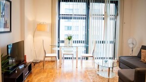 Una sala de estar moderna con una mesa de vidrio, dos sillas, un sofá, un televisor y una lámpara de pie.