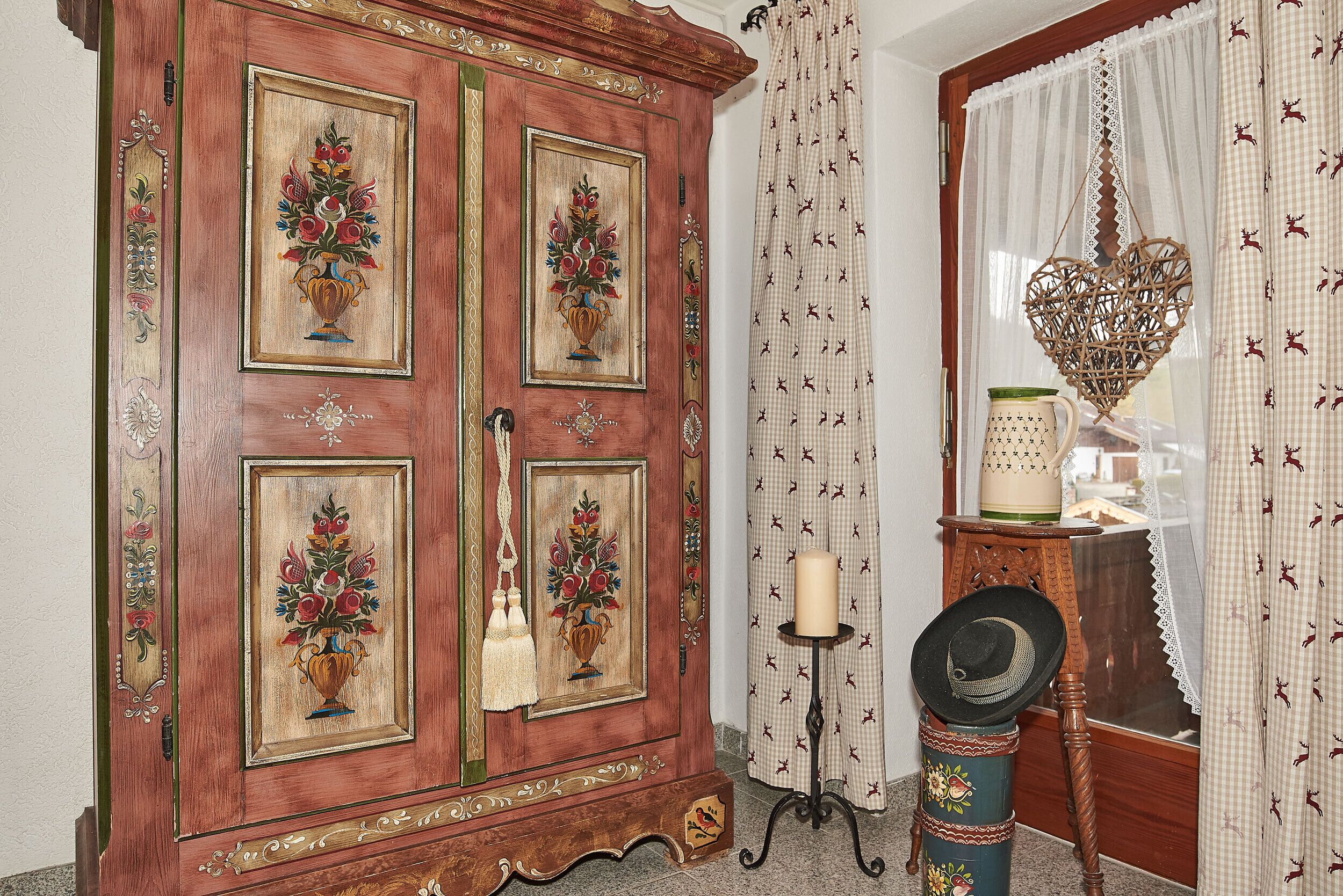 A traditional wooden cabinet with floral paintings, a candle holder, and a decorative hat on a stand.