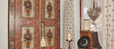 A traditional wooden cabinet with floral paintings, a candle holder, and a decorative hat on a stand.