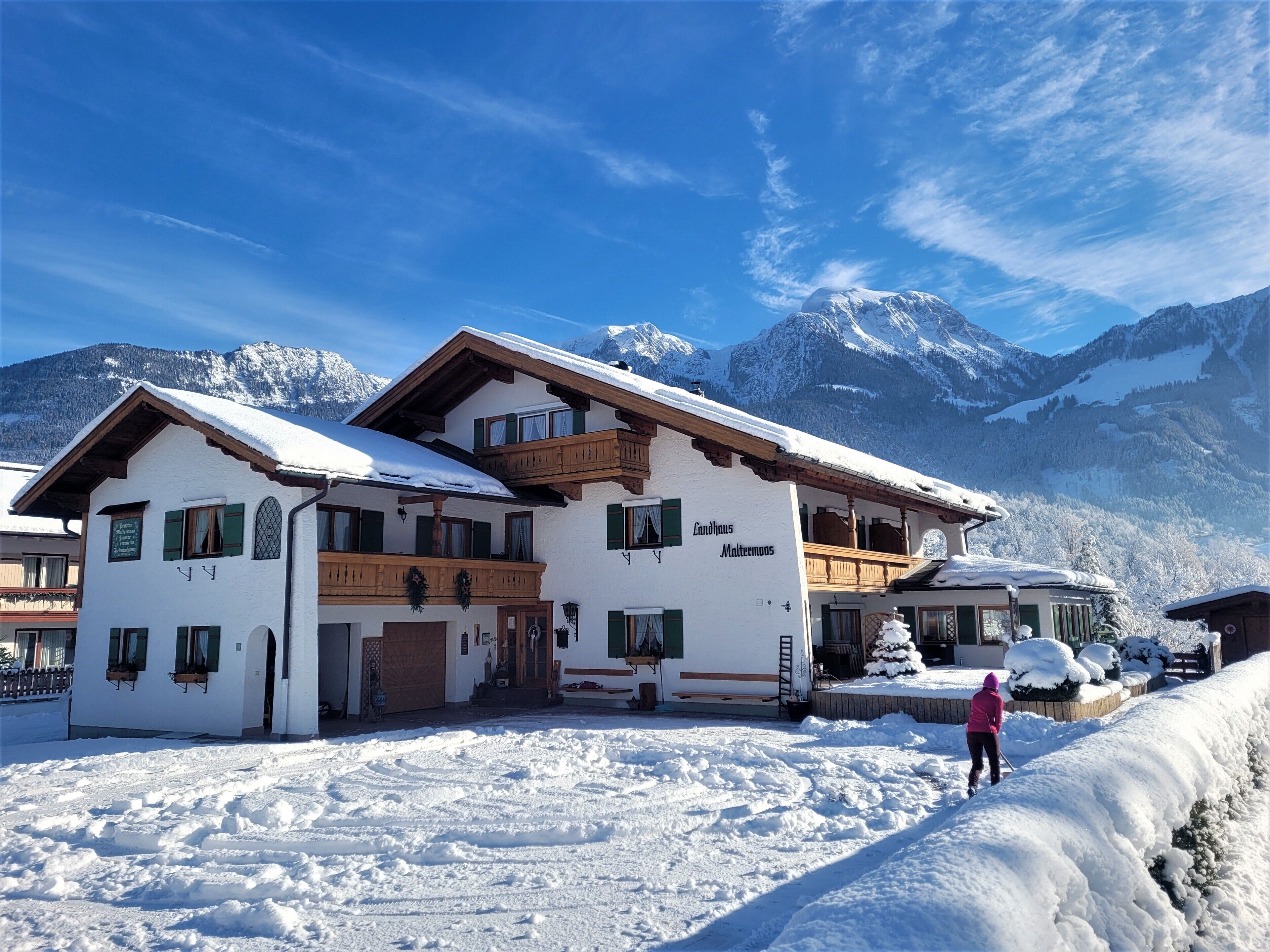 Un grand immeuble à étages, dont le toit et les balcons sont recouverts de neige, entouré d’un paysage enneigé et de montagnes.