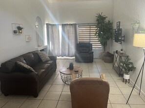 Relax in this stylish living room with a sofa, coffee table, and armchair, surrounded by artwork and plants.