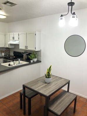 Compact kitchen with stove, sink, and modern faucet, featuring a dining area with a bench.