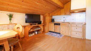 A wooden interior with a dining table, chairs, a television, kitchen cabinets, and a tiled backsplash. - Apartment 60sqm, balcony, kitchenette, 2 bedrooms, living room, max 4 p. (Ruhpolding)