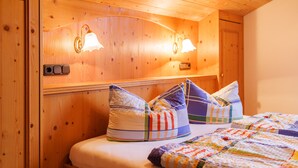 A wooden cabin-style room with a bed, colorful pillows, and wall-mounted lights. - Apartment 60sqm, balcony, kitchenette, 2 bedrooms, living room, max 4 p. (Ruhpolding)