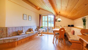 A cozy room with a wooden ceiling, a sofa, a dining table, and a chair. - Apartment 60sqm, balcony, kitchenette, 2 bedrooms, living room, max 4 p. (Ruhpolding)
