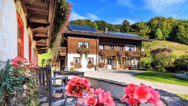 A traditional wooden building with a balcony, solar panels, and hanging flower baskets. - Apartment 60sqm, balcony, kitchenette, 2 bedrooms, living room, max 4 p. (Ruhpolding)