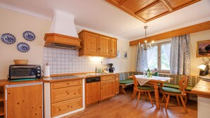 A compact kitchen with wooden cabinets, a built-in dishwasher, and a dining area with a table and chairs. - Fewo , Balkon, Kochnische, 2 Schlaf- und 1 Wohn-/schlafzimmer, max 5 Personen (Ruhpolding)