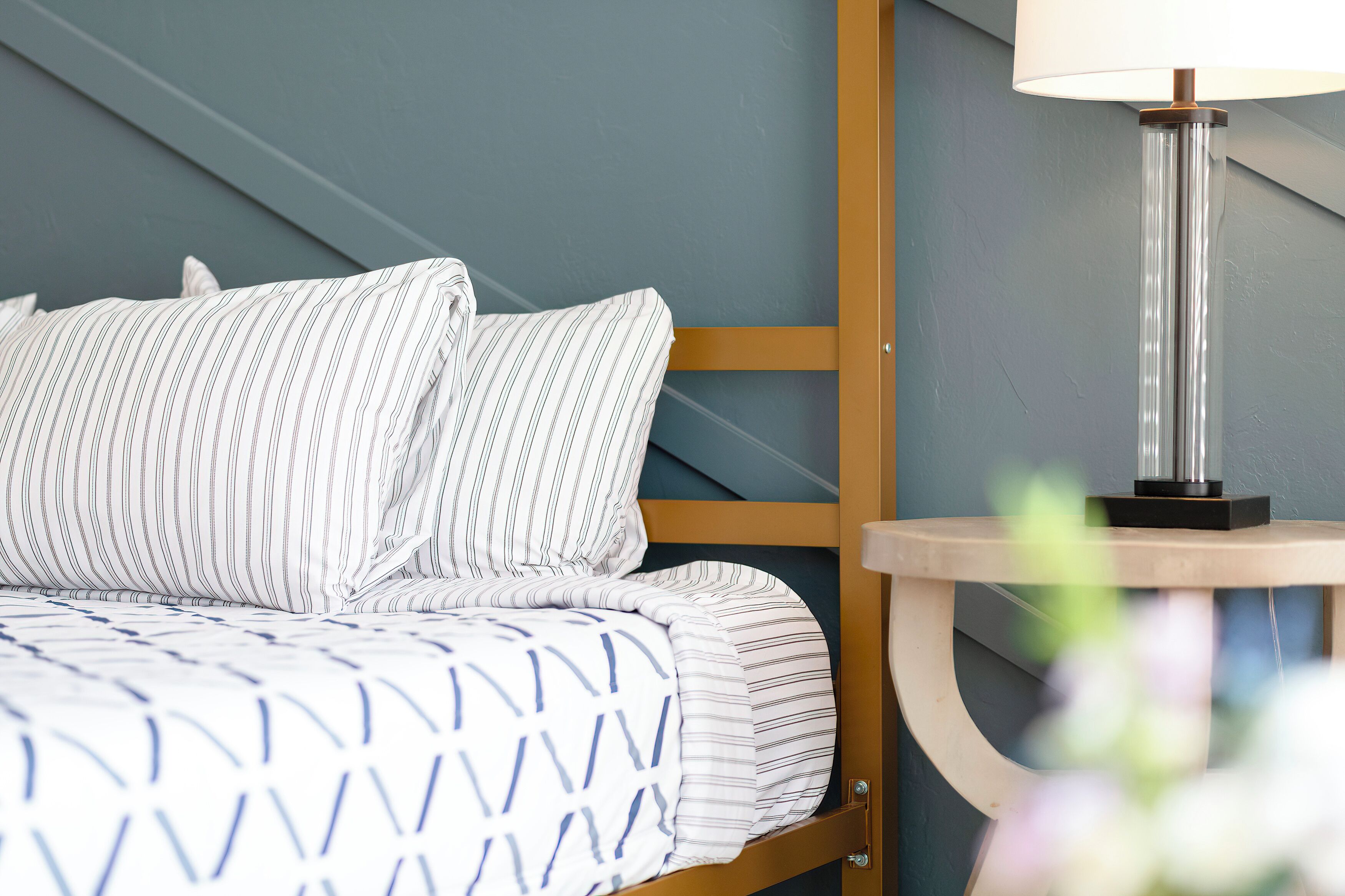 A neatly made bed with striped bedding, a bedside table with a lamp, and a blue wall.
