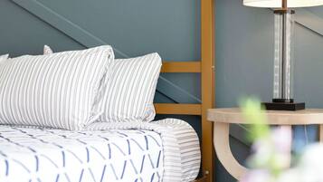 A neatly made bed with striped bedding, a bedside table with a lamp, and a blue wall.