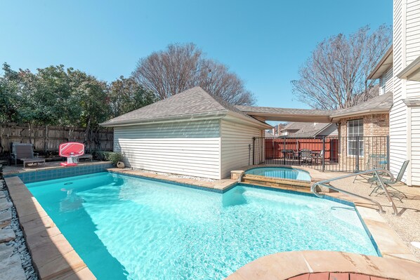 Patio trasero con piscina, canasta de baloncesto y zona de estar exterior con mobiliario.