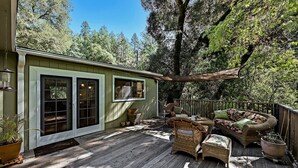 Eine Holzterrasse mit Korbmöbeln, ein kleines Gebäude mit Fenstern und ein Baum im Hintergrund.