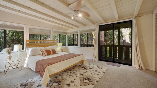 Ein Schlafzimmer mit einem großen Bett, einem Deckenventilator und Blick ins Freie durch eine Schiebetür.