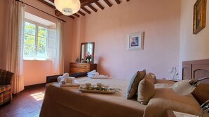 Un dormitorio con cama, una silla, cómoda, espejo y ventana con cortinas.