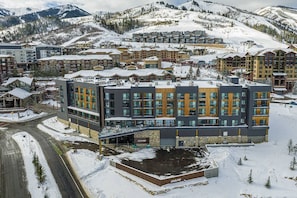 Un hôtel moderne à plusieurs étages, avec une station de ski en arrière-plan et un paysage enneigé.