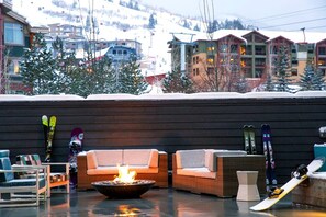 A snow-covered outdoor seating area with a fire pit, lounge chairs, and skis. - Canyon Haus 223 (Park City)