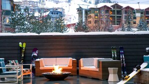 A cozy outdoor seating area with a fire pit, wicker furniture, and skis leaning against a wall.