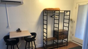 Une petite pièce, de dimensions réduites, avec une table en bois et deux chaises noires, un lit superposé en métal muni d’une étagère suspendue, et une porte dotée d’un panneau en verre dépoli.