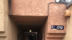 Une entrée fermée par un portail mène à un immeuble dont la façade présente un relief particulier et sur lequel on peut voir un panneau indiquant le numéro 1712.