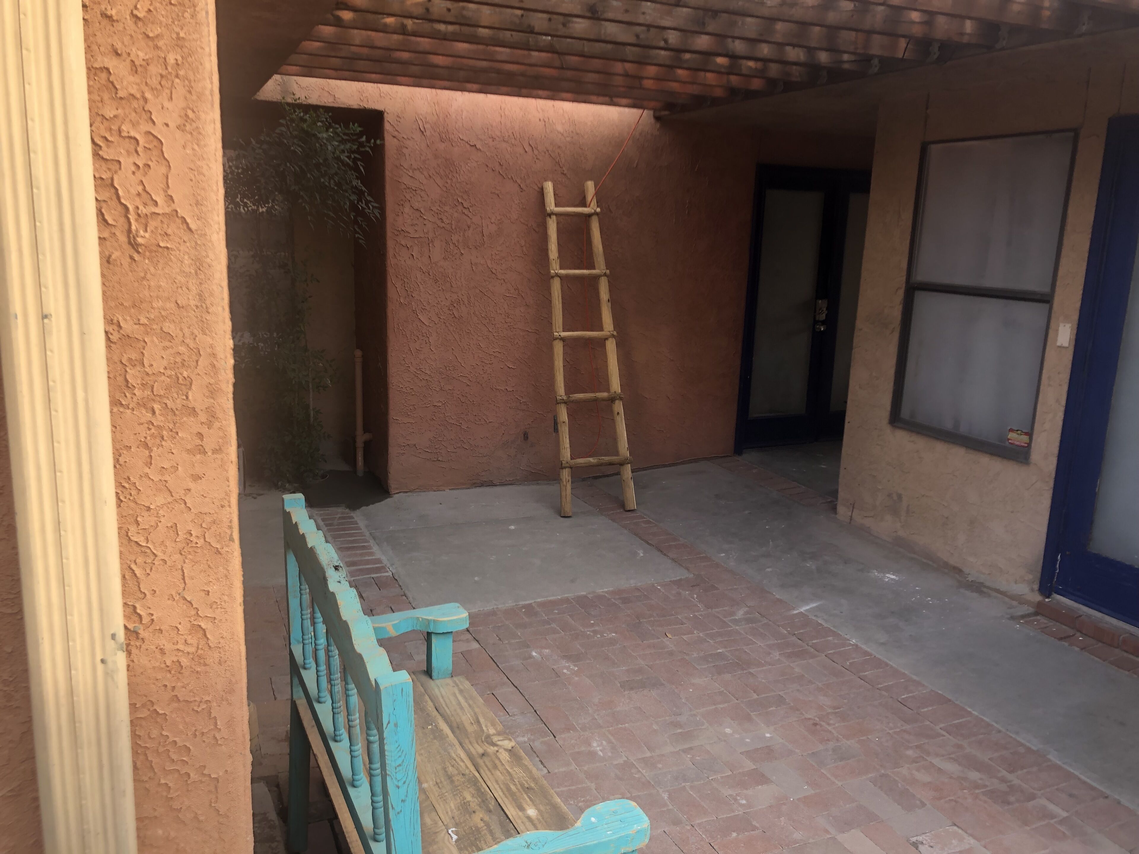 A covered outdoor area with a wooden bench, a ladder, and a door leading to another room.