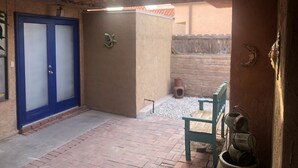 Un patio abrité avec une porte bleue, un petit élément décoratif fixé au mur et un banc rustique.
