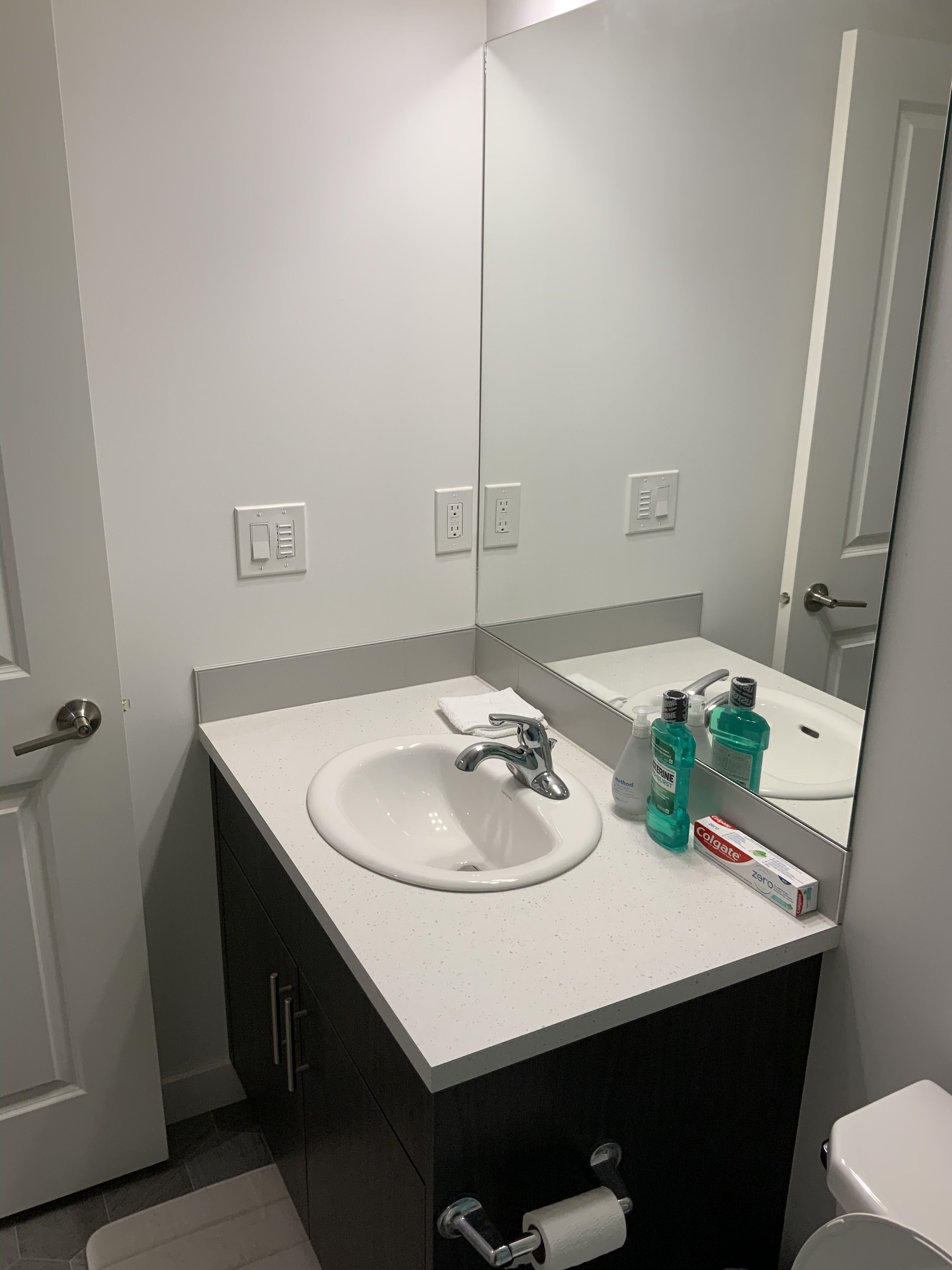 Een moderne badkamer met een witte wastafel, een spiegel en toiletartikelen.