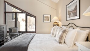 A bedroom with a large window, a bed with multiple pillows, a bedside table, and a chair. - Cloud 9 by AvantStay | Located at the Base of Vail Ski Resort w/ Fire Pit + BBQ (Vail)