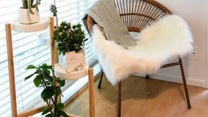 A room with a wooden floor, a white chair with a fluffy seat, a wooden plant stand with multiple potted plants, and a painting on the wall. - King 1BR, Steps to the Beach on Walk St with Patio and Garden, Prime Location (Venice)