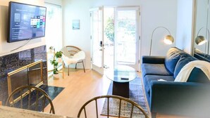 A modern living room with a flat-screen TV, a sofa, a coffee table, and a dining area with chairs. - King 1BR, Steps to the Beach on Walk St with Patio and Garden, Prime Location (Venice)
