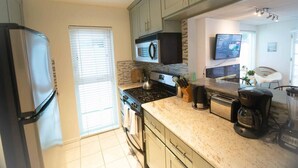 A modern kitchen with a refrigerator, stove, microwave, and coffee maker. - King 1BR, Steps to the Beach on Walk St with Patio and Garden, Prime Location (Venice)