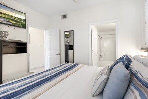 A bedroom with a bed, a TV, a wardrobe, and a bathroom visible through an open door.