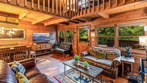 A wooden cabin interior with a dining area, sofa, and a television.