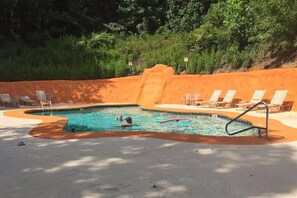 Une piscine bordée de sable, entourée de chaises longues et d’une terrasse en béton.