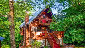 A rustic cabin with a stone foundation, a wooden deck, and a red staircase leading to the entrance.