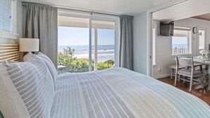 A bedroom with a large bed, a desk, and a view of the ocean. - Oceanfront- Sea Gem Cottage (South Beach)