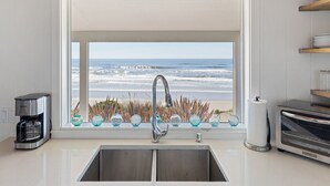 A kitchen with a view of the ocean, a coffee maker, a toaster, and a window with decorative glass spheres. - Oceanfront- Sea Gem Cottage (South Beach)