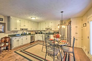 Una cocina con armarios blancos, una mesa de comedor con sillas, un tapete y un refrigerador.