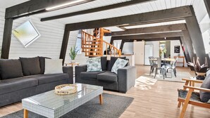 Un loft modern amb biges de fusta al descobert, una taula de cafè de vidre, un sofà i una zona de menjador amb cadires i una taula.