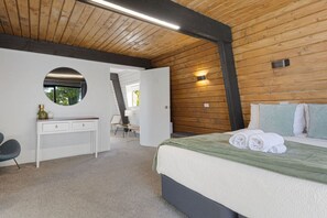 Een slaapkamer met een bed, een bureau, een stoel, een ronde spiegel en een raam.