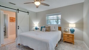 Ein Schlafzimmer mit einem Bett, einem Nachttisch, einer Lampe, einem Deckenventilator, einem Fenster und einer Tür.