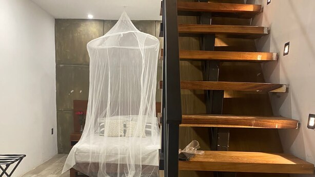 Un dormitorio moderno con una escalera de madera, una cama con dosel blanco y una pequeña mesa con una silla.