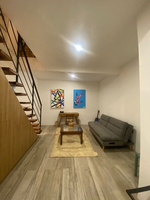 A living room with a wooden staircase, a gray sofa, a coffee table, and two abstract paintings on the wall.
