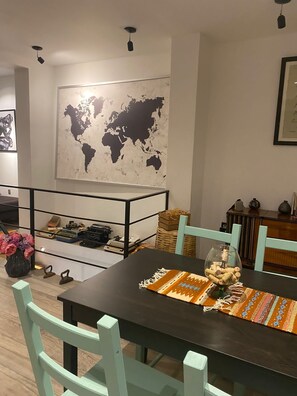 A dining area with a dark wooden table, light green chairs, a world map on the wall, and a small side table with vintage items.