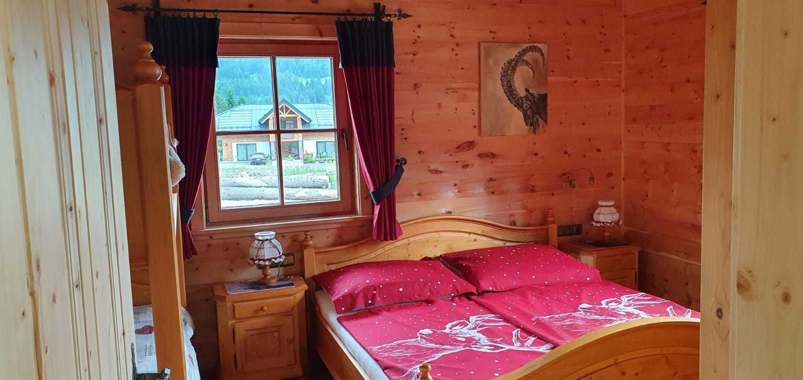 Ett sovrum i en stuga med träpanel, en säng, sängbord, ett fönster med gardiner och utsikt över bergen.