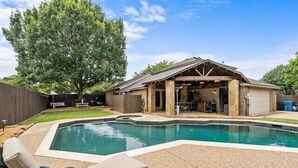 Un jardin avec une piscine, un patio couvert et une clôture en bois.