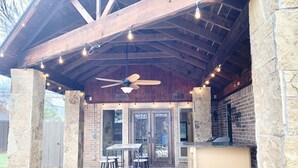 Une terrasse extérieure avec des piliers en pierre, un ventilateur de plafond et des guirlandes lumineuses.