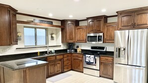 Une cuisine dotée de meubles en bois, d’appareils électroménagers en acier inoxydable, d’un grand îlot central et d’une fenêtre offrant une belle vue.