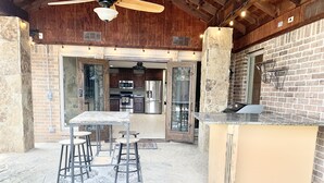 Un espace cuisine extérieur doté d’un plan de travail en pierre, de tabourets et d’une table.