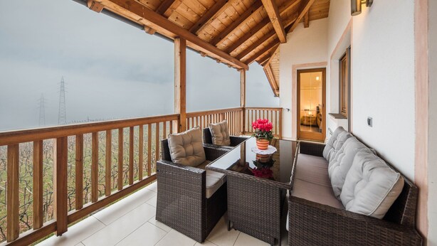 A balcony with wicker furniture, a glass table, and a view of power lines. - Apartment "Huck" with Mountain View, Balcony & Wi-Fi (Karneid)