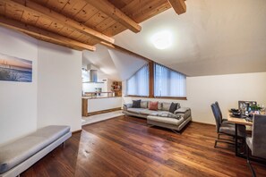 A loft-style living space with a wooden ceiling, a sofa, a dining table, and a kitchen in the background. - Apartement "Huck" with Mountain View, Balcony & Wi-Fi (Karneid)