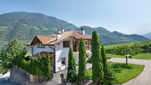 A house with a sloped roof, wooden balcony, and a stone wall. - Apartment "Huck" with Mountain View, Balcony & Wi-Fi (Karneid)